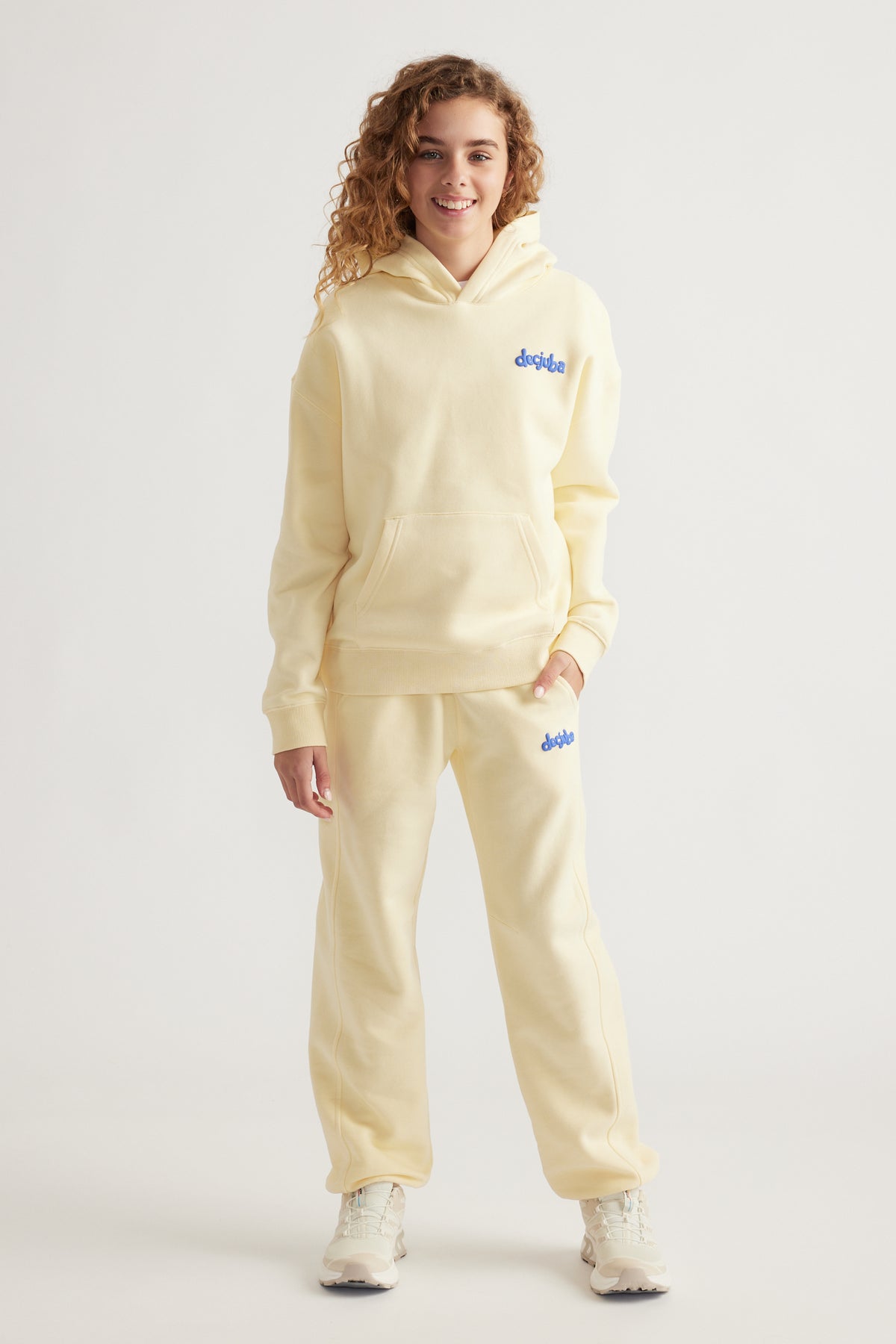Girl wearing a soft cream oversized hoodie and matching fleece pants with subtle blue logo and white sneakers