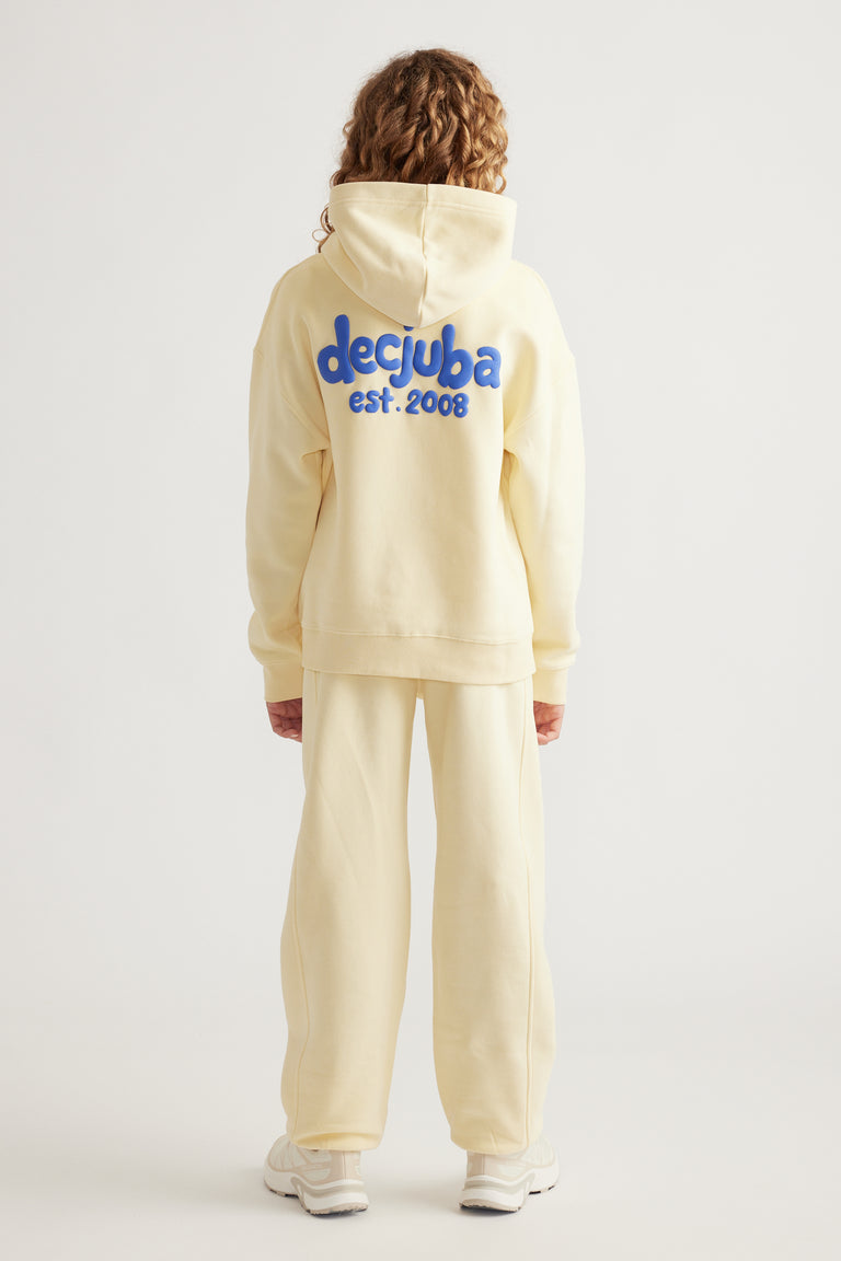 Girl wearing a cream oversized hoodie with blue branding on the back paired with matching wide-leg pants and sneakers