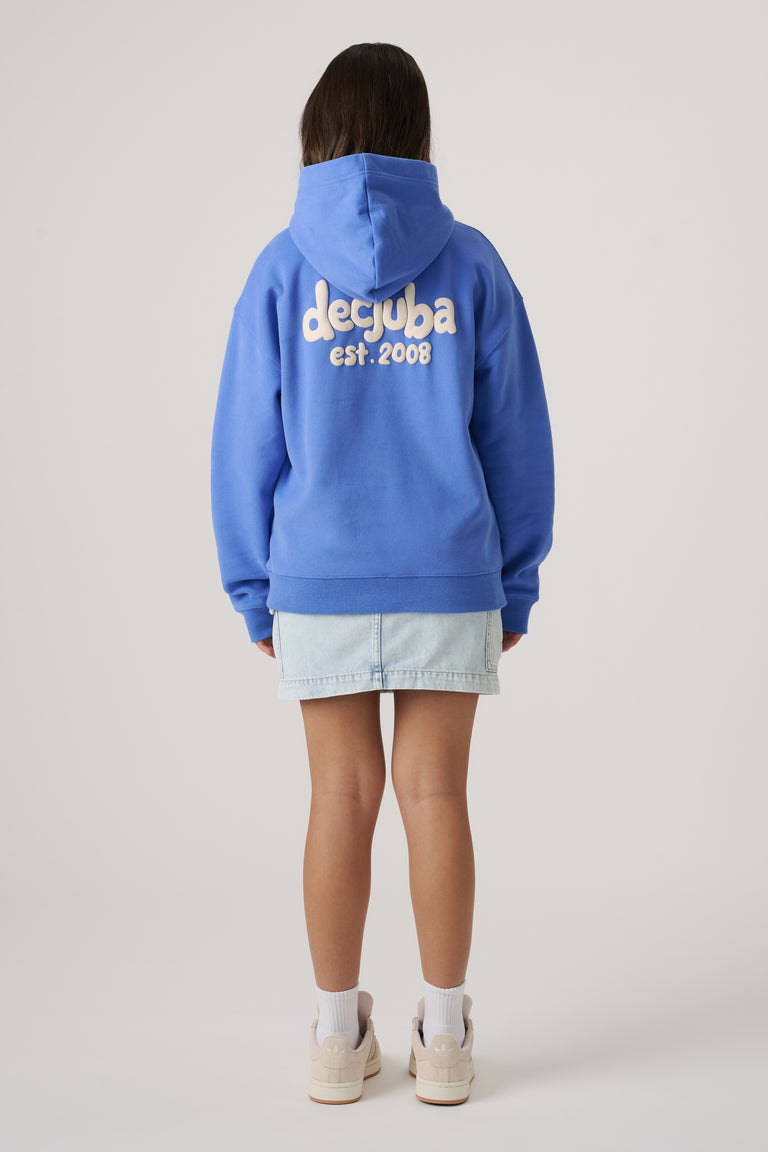 Girl wearing a blue oversized hoodie with logo lettering on the back paired with a light denim skirt and sneakers