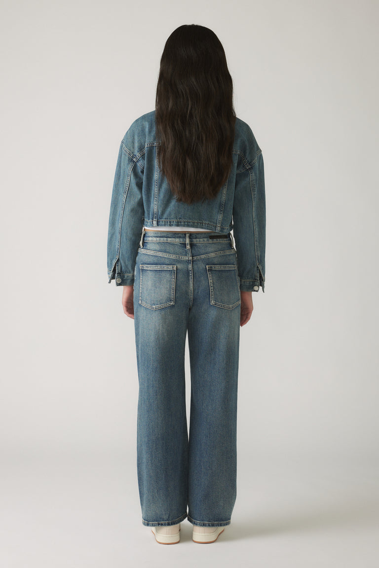 Back view of a girl wearing a cropped blue denim jacket paired with straight leg denim jeans and white sneakers