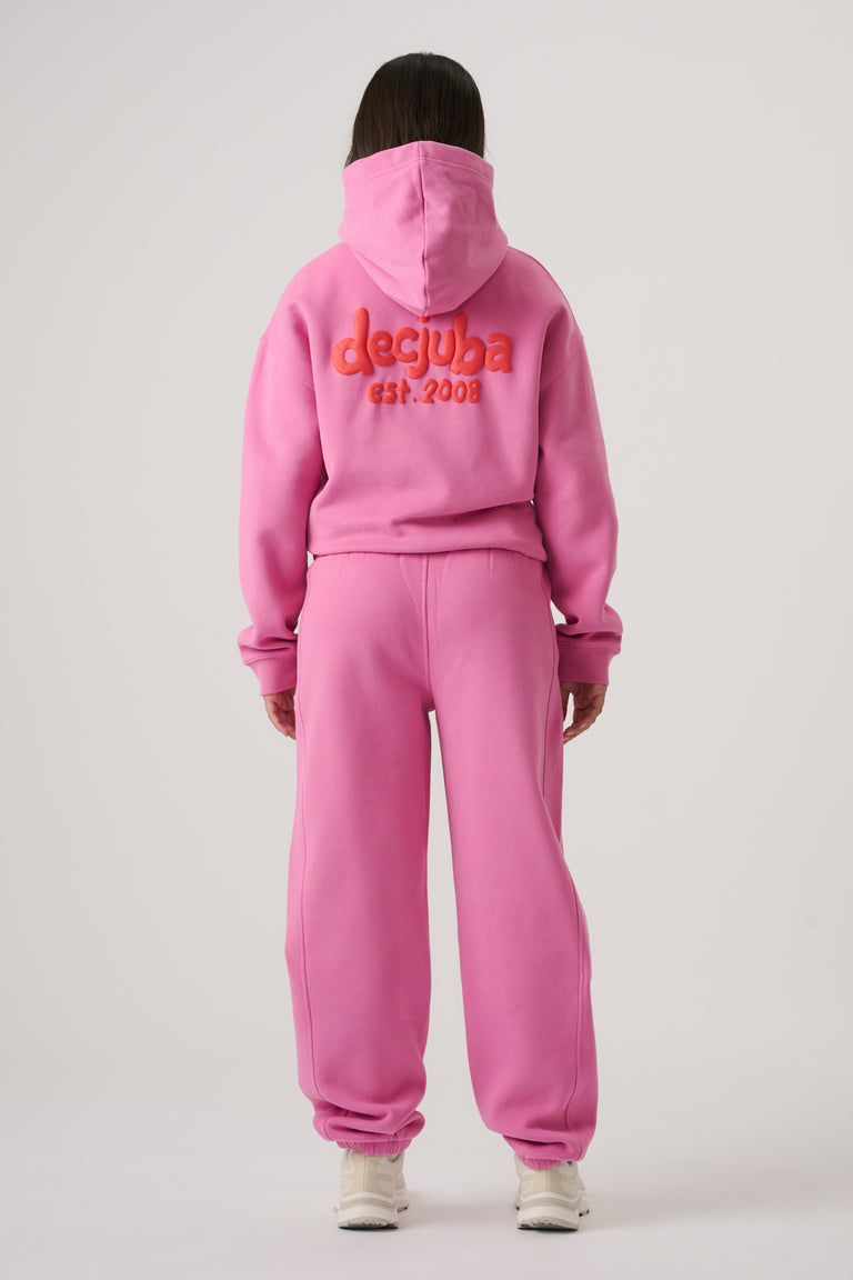 Girl wearing bright pink balloon leg trackpants paired with matching hoodie featuring bold logo on the back