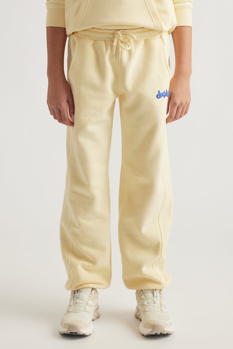 Teen girl wearing pale yellow balloon leg trackpants with elastic waist, side pockets, and casual sneakers