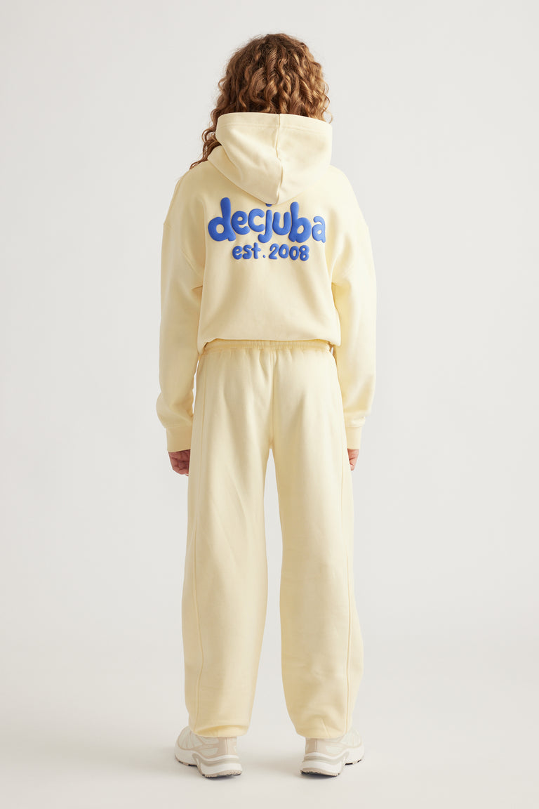 Teen girl wearing a cream hooded sweatshirt with blue logo and matching relaxed fit track pants with cuffed hems