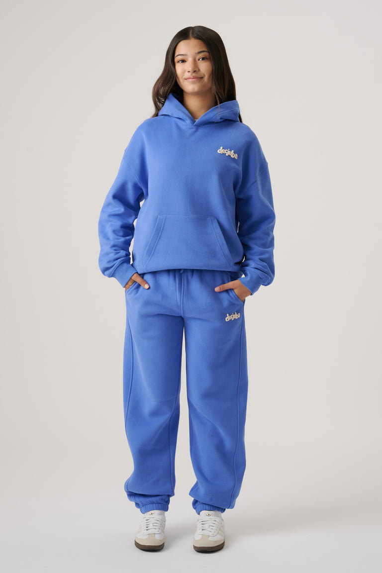 Teen girl wearing relaxed blue balloon leg trackpants with matching hoodie and white sneakers