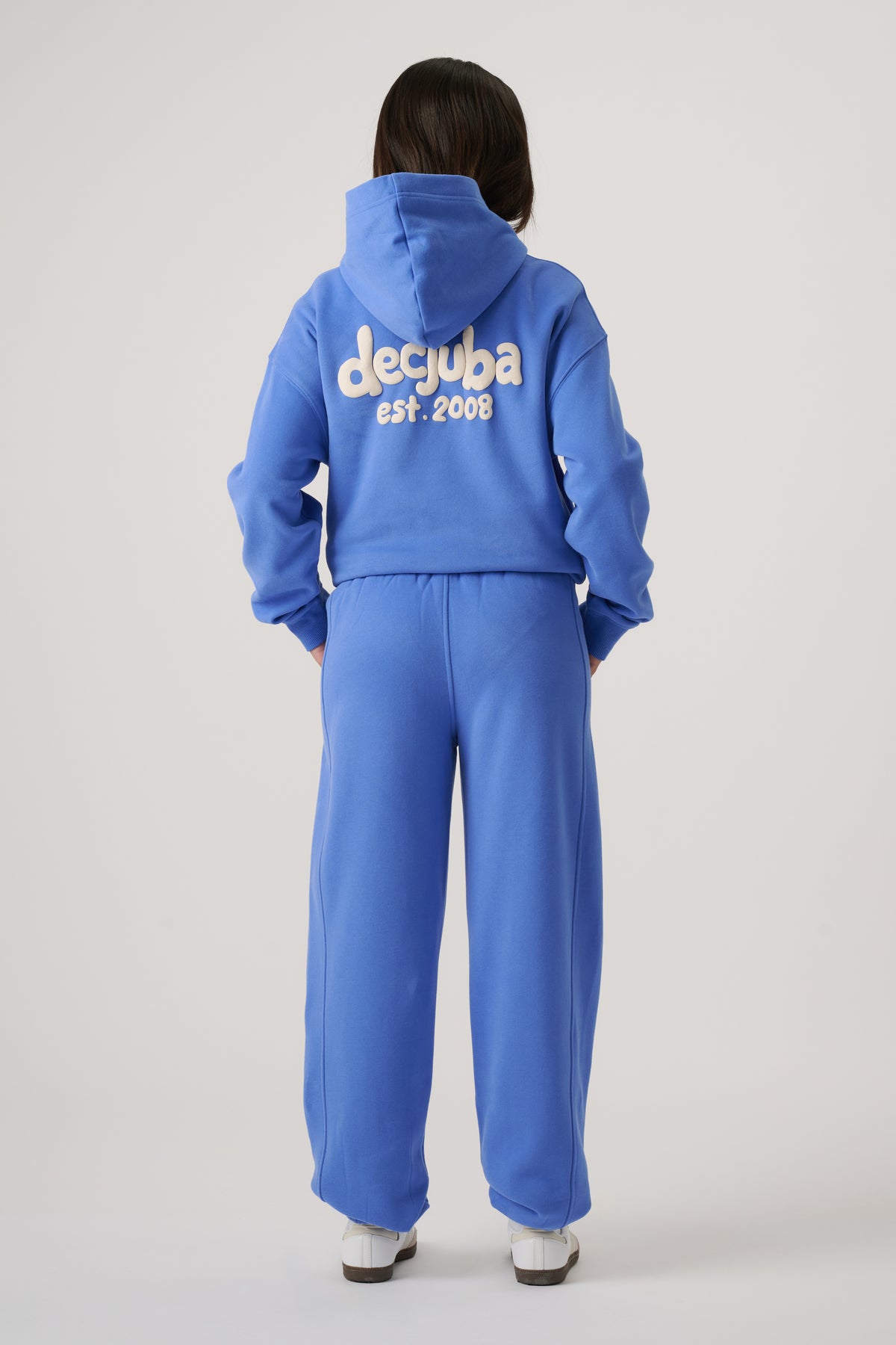 Girl wearing bright blue hoodie with logo text on back paired with matching loose-fitting balloon leg pants and white shoes
