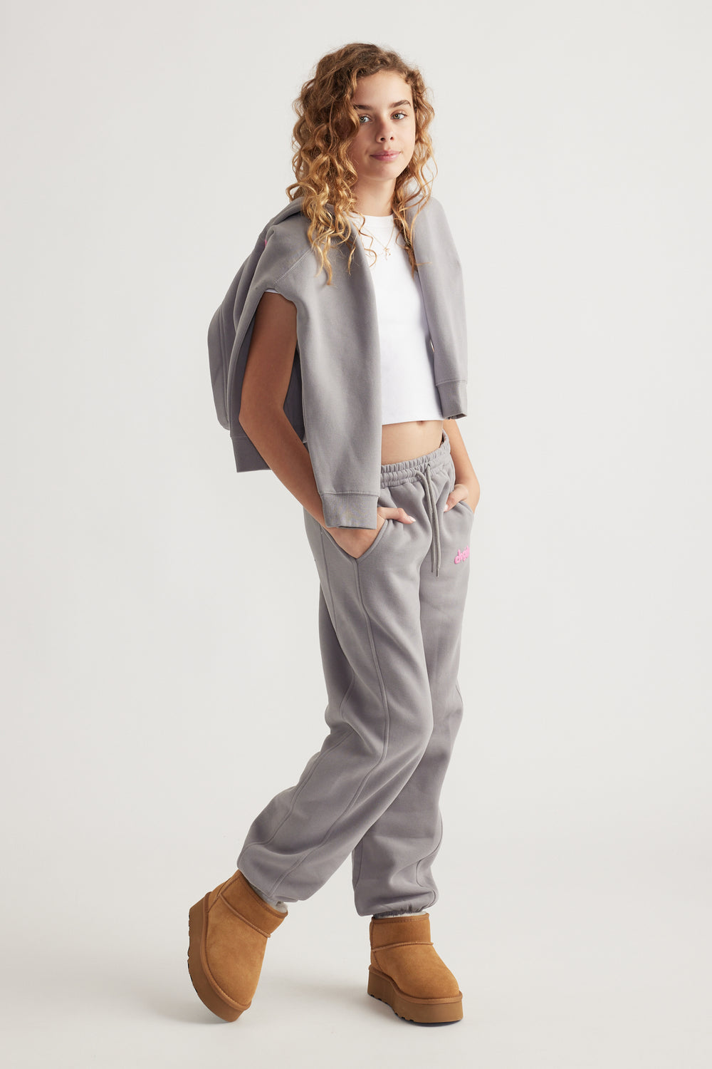 Teen girl wearing relaxed grey balloon leg pants with elastic waist and side pockets paired with tan boots