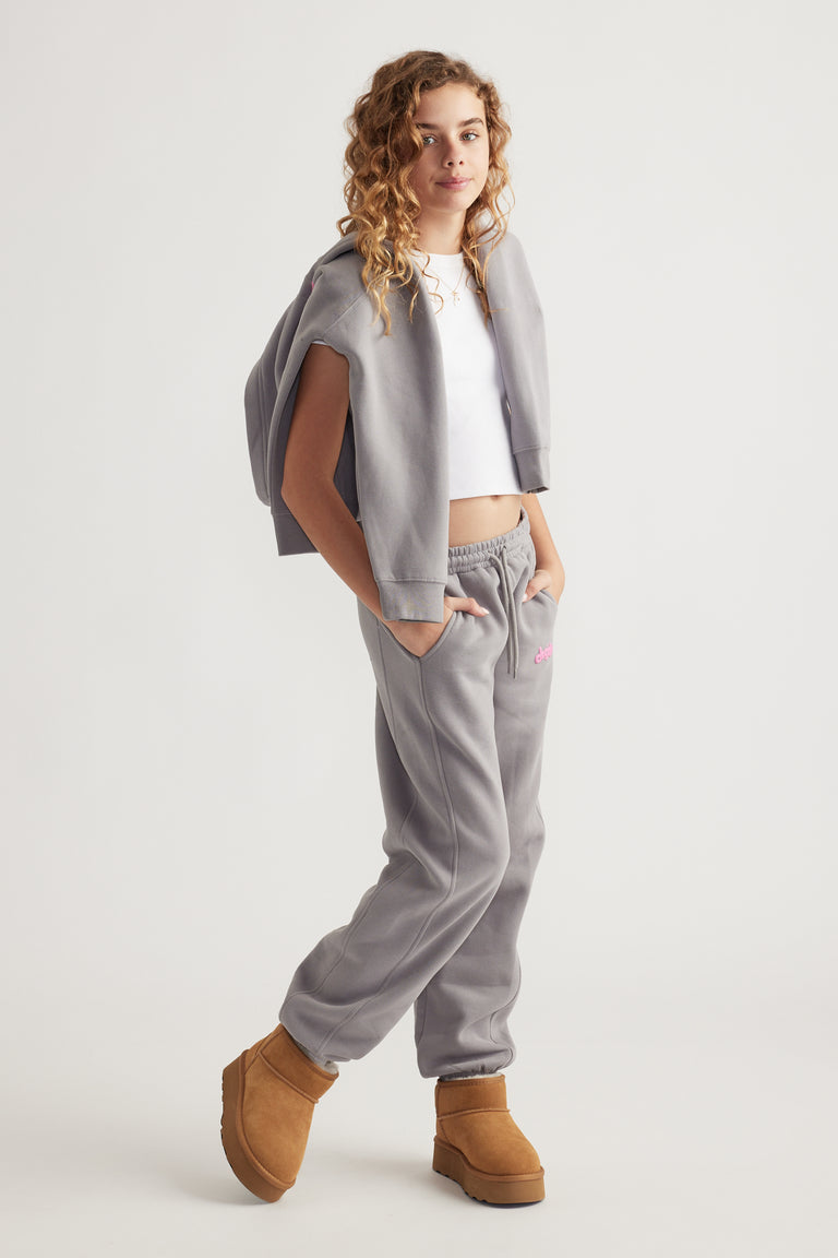 Teen girl wearing relaxed grey balloon leg pants with elastic waist and side pockets paired with tan boots