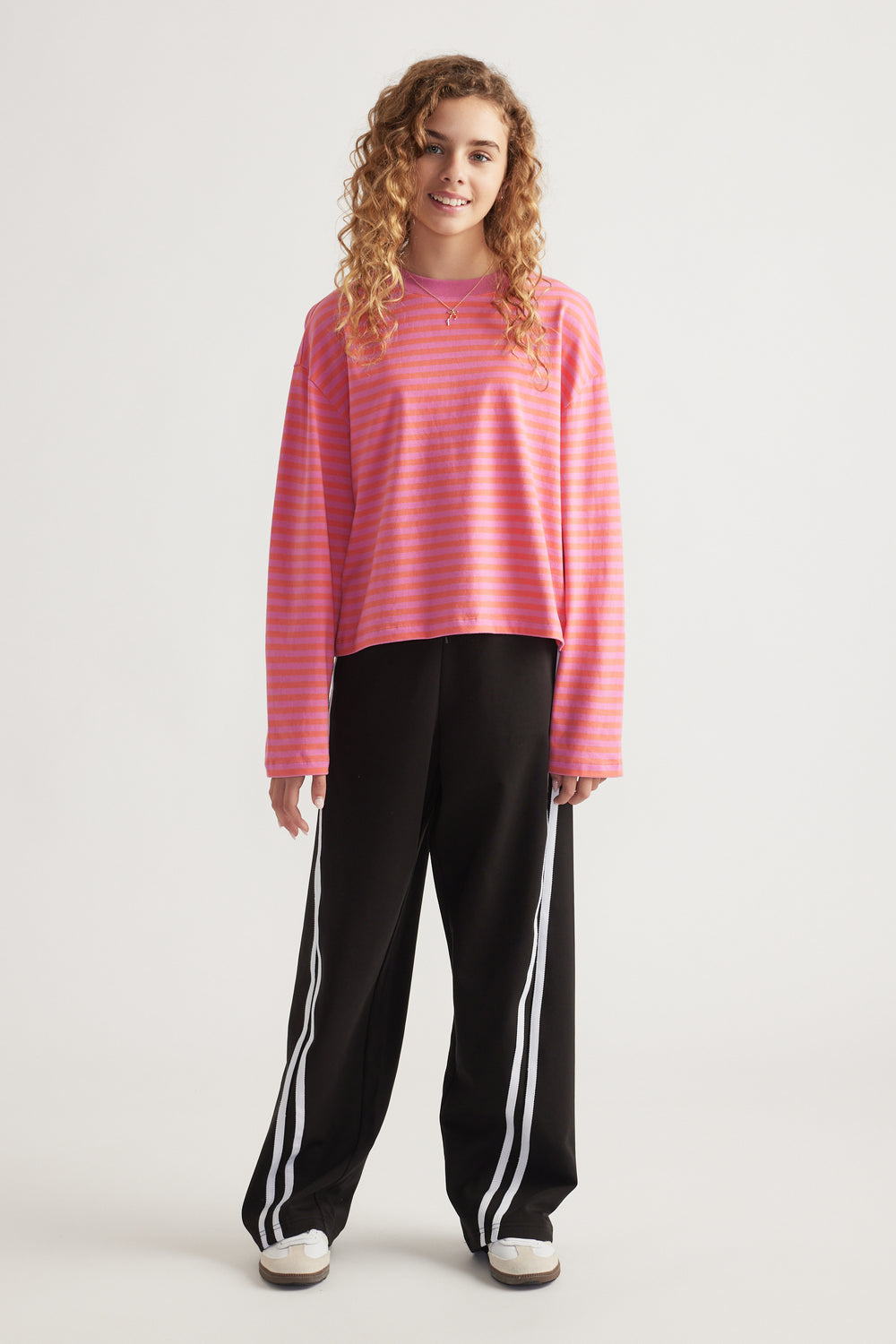 Teen girl wearing a relaxed fit, long sleeve pink striped top paired with black wide-leg pants with side stripes