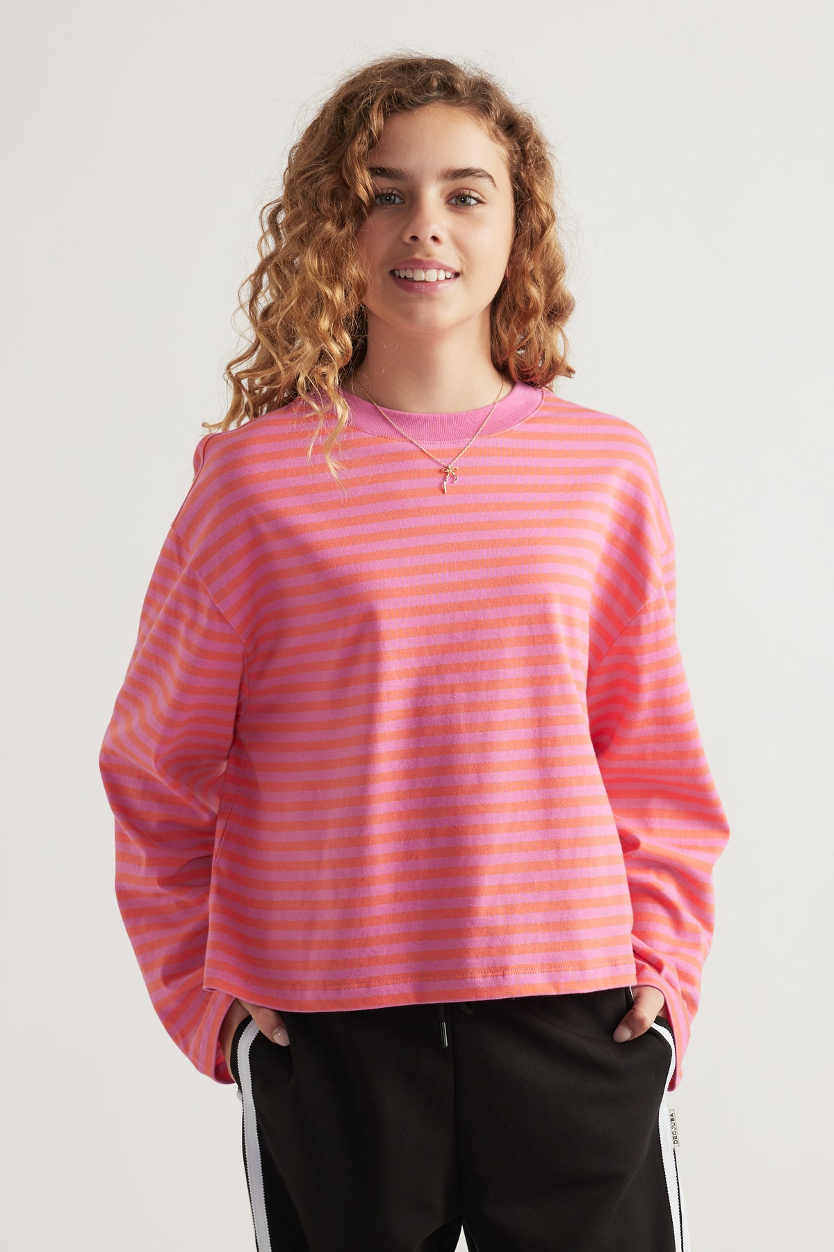 Girl wearing a relaxed fit long sleeve striped top in pink and orange paired with black pants with side stripes
