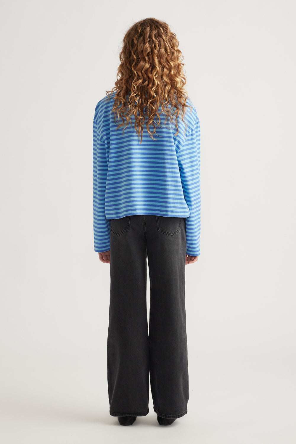 Girl wearing a blue striped long sleeve boxy tee paired with wide-leg black denim jeans, viewed from behind