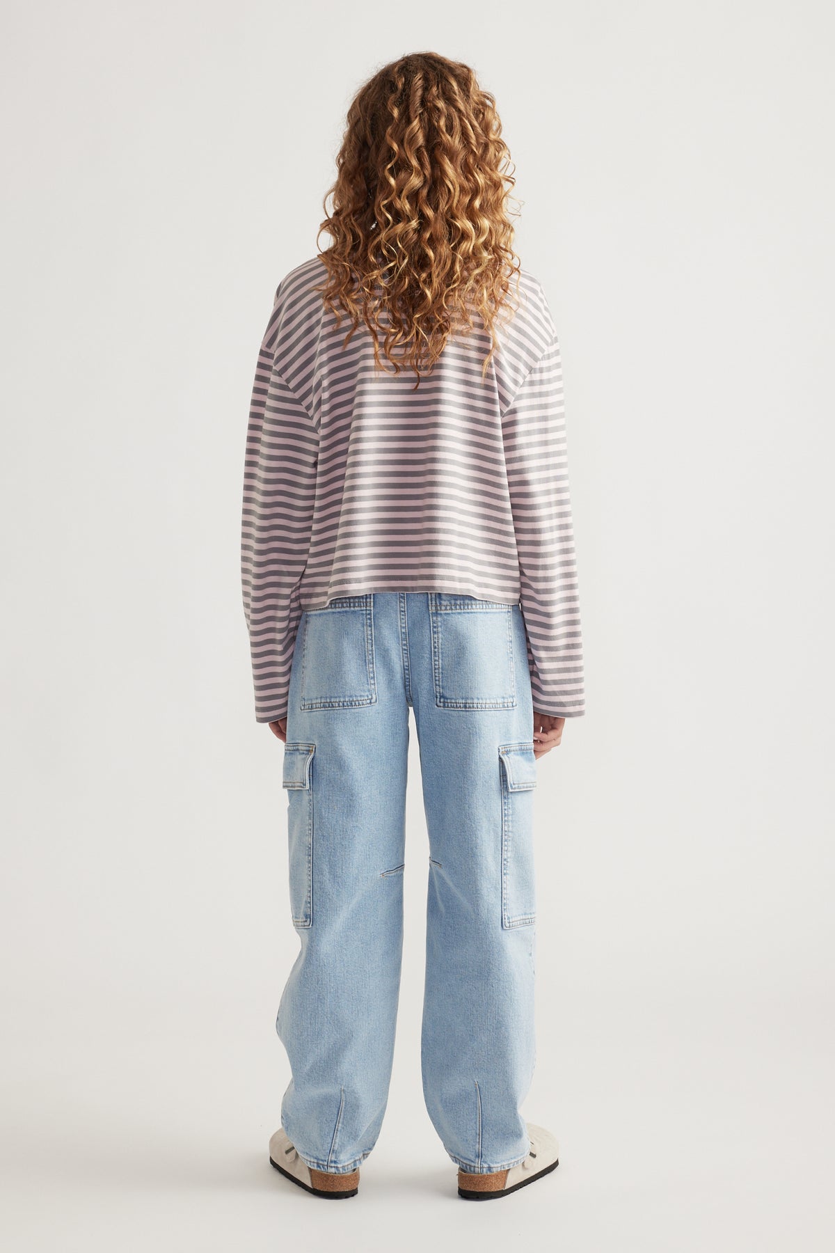 Girl with curly hair wearing a relaxed striped long sleeve top and light wash cargo jeans with wide legs and pockets