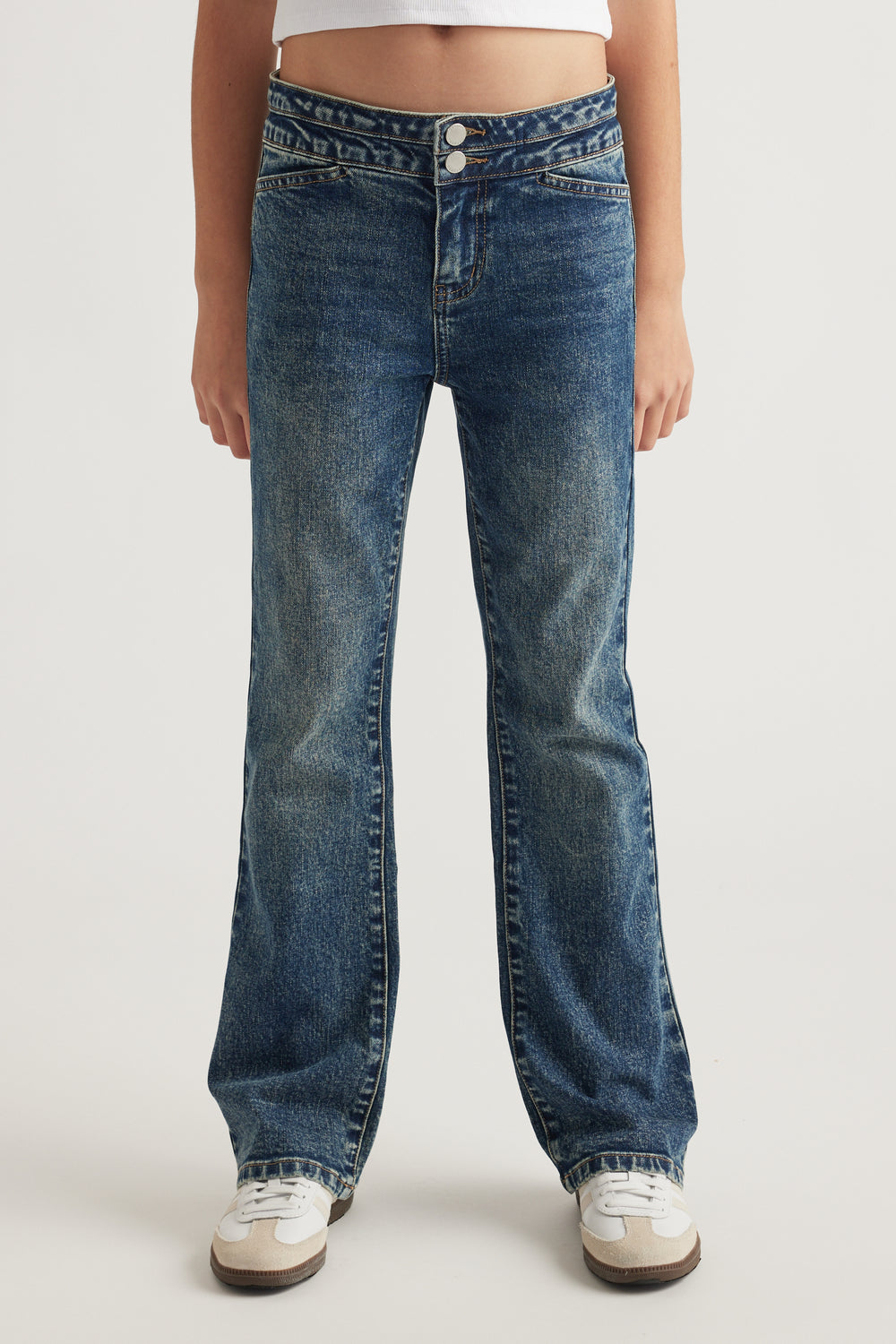 Front view of teen wearing low-rise bootcut jeans in faded dark denim with double button closure and white sneakers