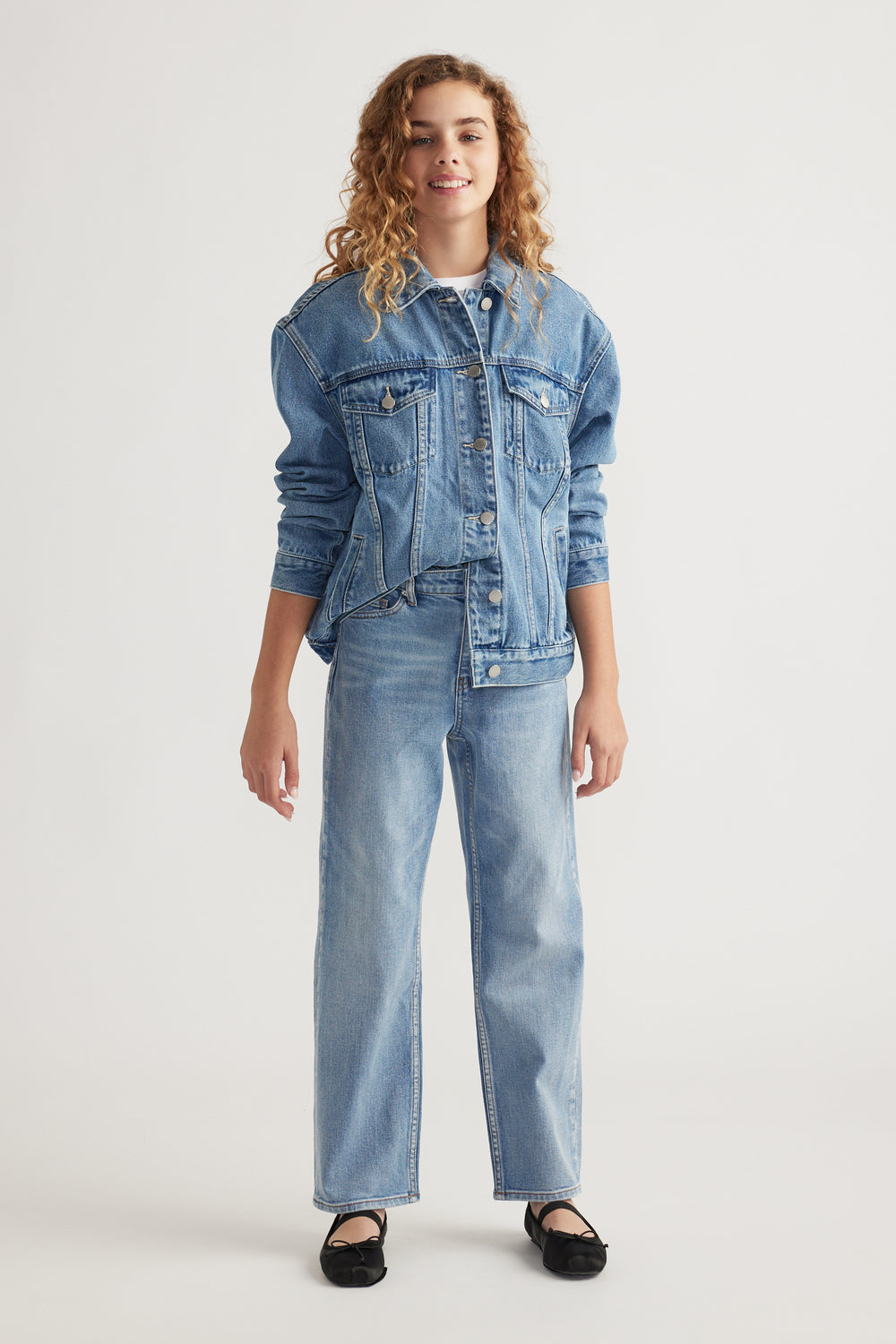 Teen girl wearing light wash straight leg jeans paired with matching denim jacket and black flats