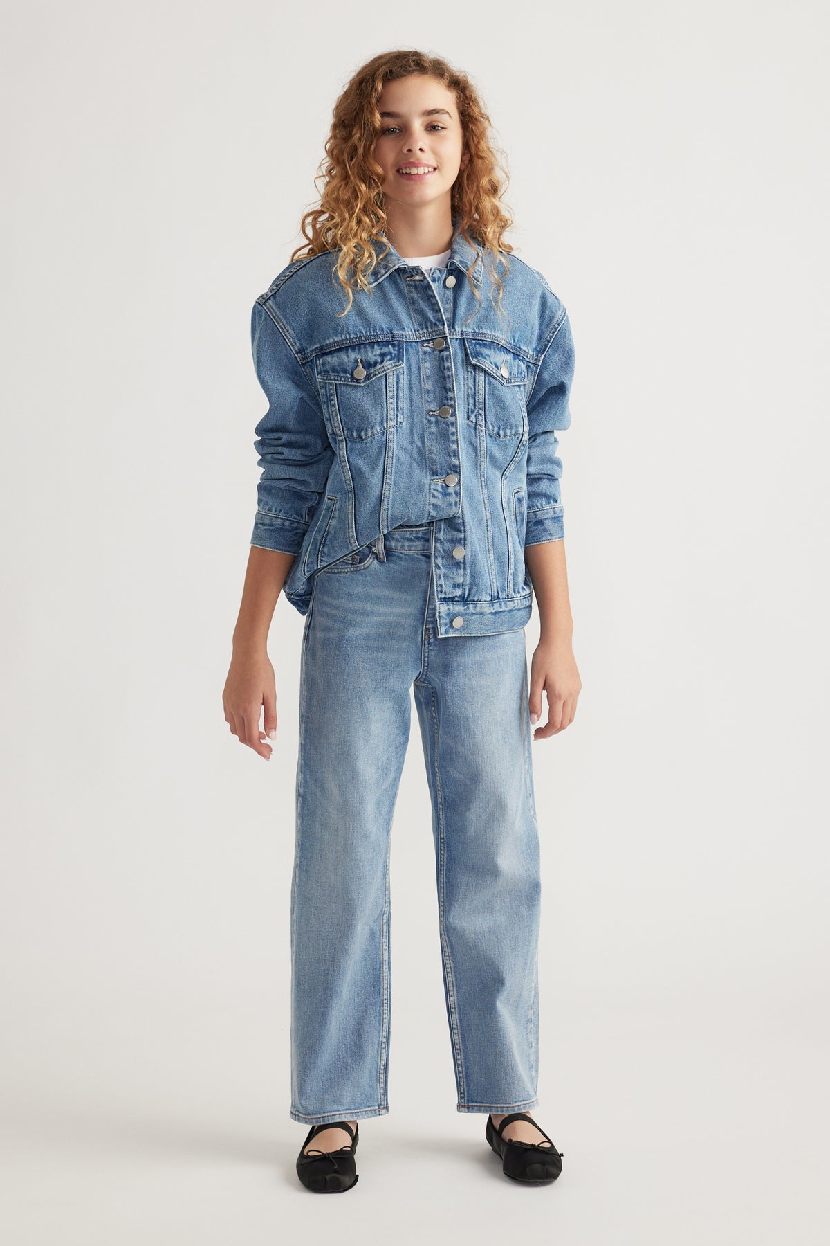 Teen girl wearing light wash straight leg jeans paired with matching denim jacket and black flats