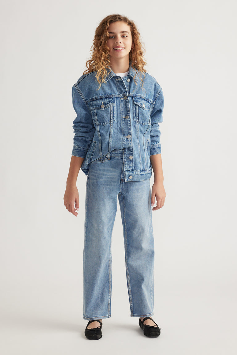 Teen girl wearing light wash straight leg jeans paired with matching denim jacket and black flats