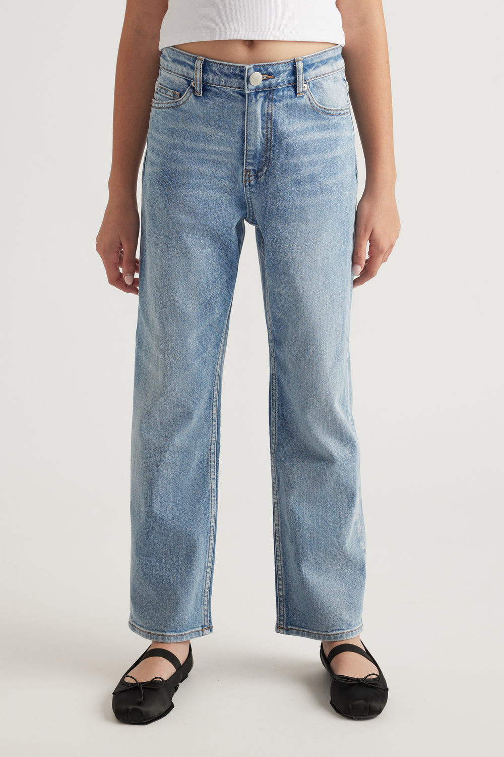 Front view of teen wearing light wash mid-rise straight leg jeans paired with black ballet flats