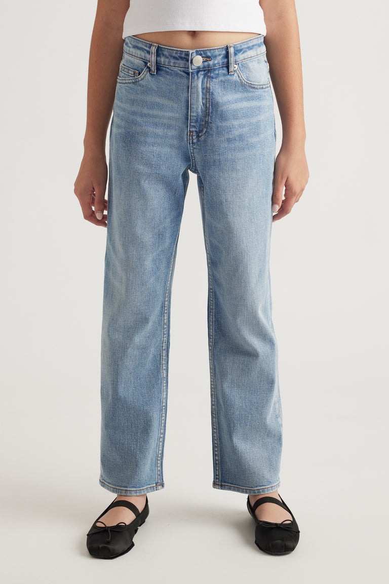 Front view of teen wearing light wash mid-rise straight leg jeans paired with black ballet flats
