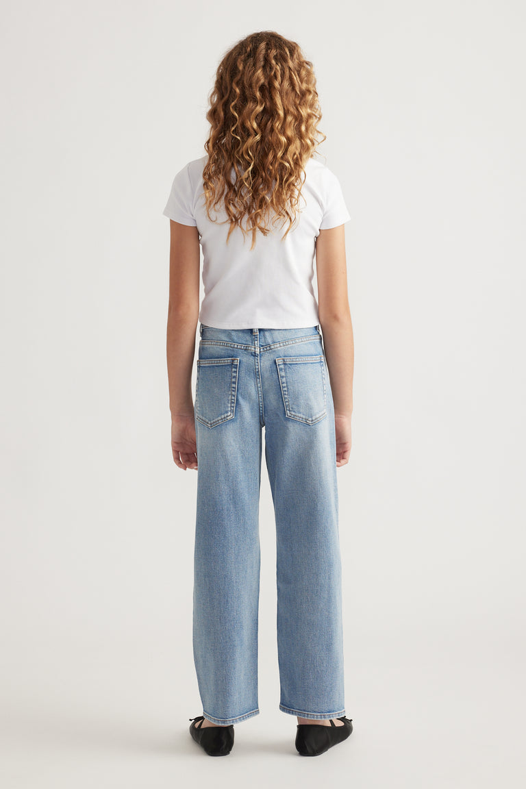 Rear view of teen wearing mid-rise light blue straight leg jeans with back pockets and a white short sleeve top