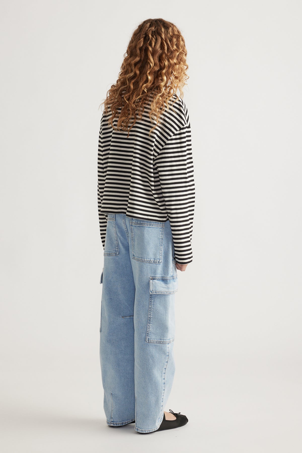 Girl wearing light wash cargo jeans with patch pockets paired with a black and white striped long-sleeve top and black flats