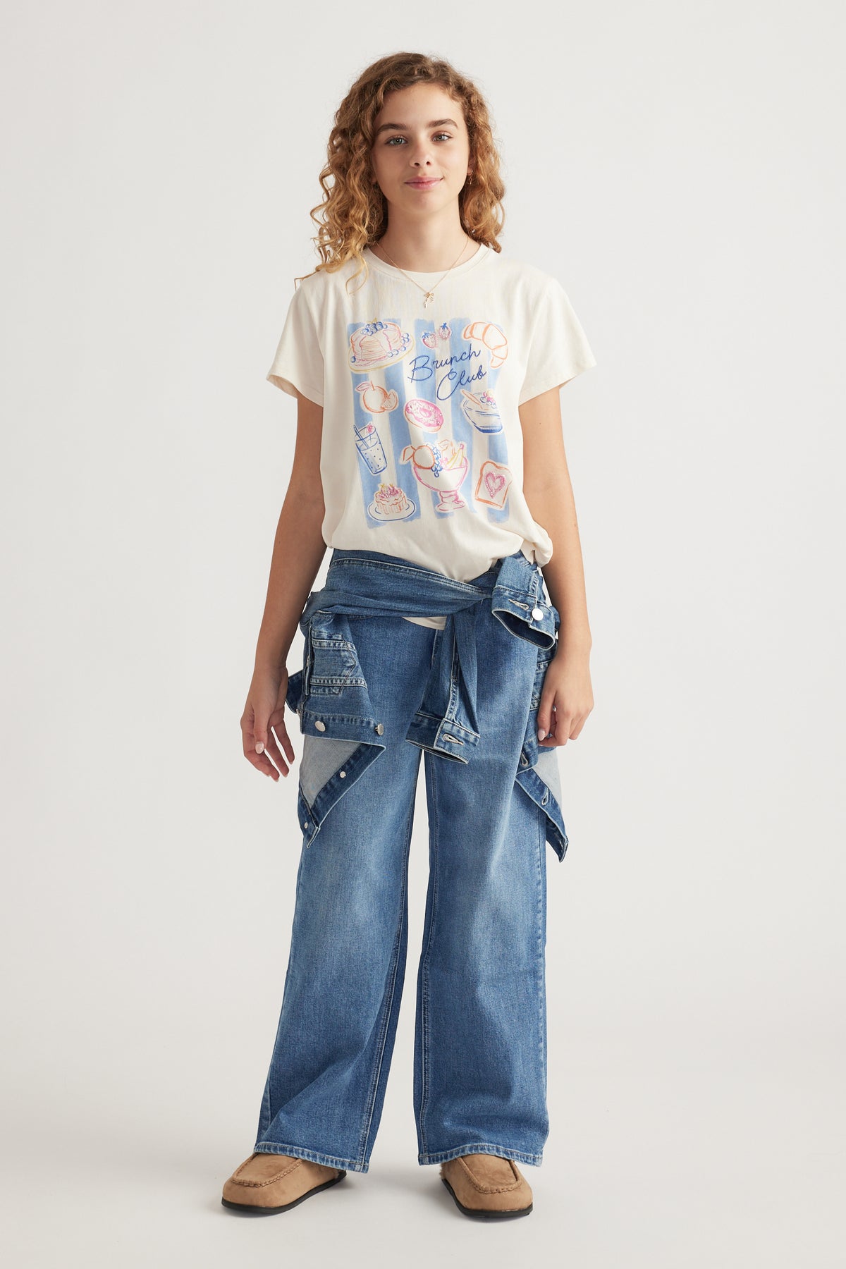 Teen girl wearing a printed cream tee with casual blue wide-leg denim jeans and a denim jacket tied around waist