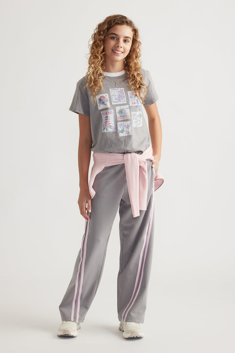 Girl wearing a printed short sleeve tee with city-themed artwork paired with grey track pants and pink sweater tied at waist