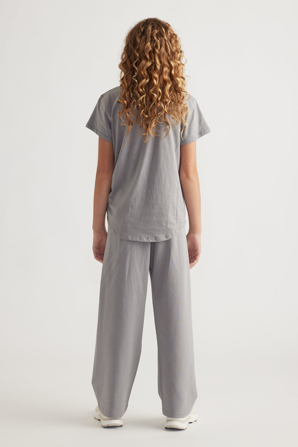 Rear view of girl wearing loose grey tee with curved hem and matching wide-leg pants and white sneakers