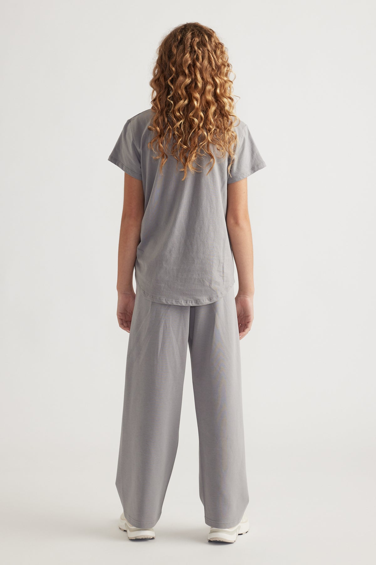 Rear view of girl wearing loose grey tee with curved hem and matching wide-leg pants and white sneakers