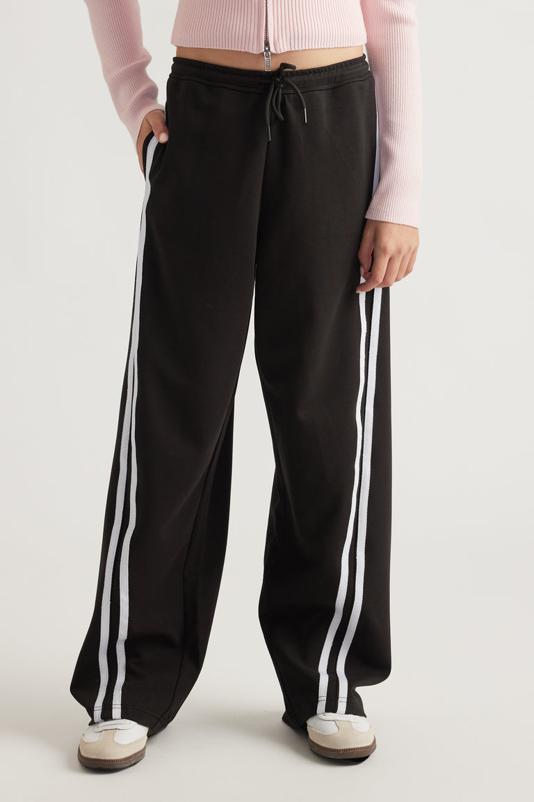 Teen wearing black wide-leg track pants with white side stripes and a drawstring waist paired with casual sneakers