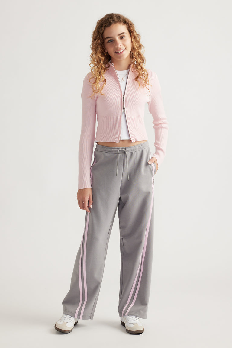 Teen girl wearing grey wide-leg pants with pink side stripes and a pale pink zip-up cardigan over white top
