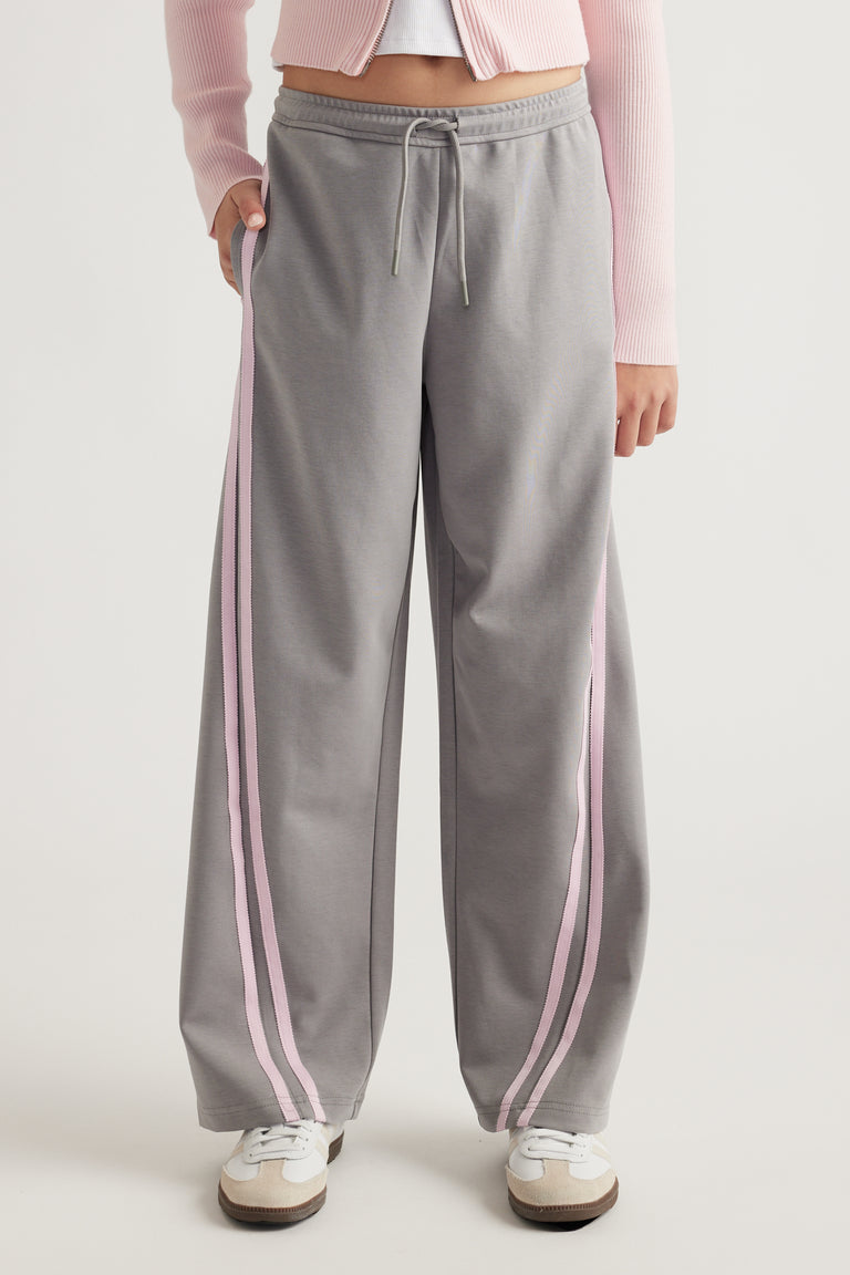 Teen wearing wide-leg grey pants with pink side stripes and elasticated waist paired with white sneakers and pink top