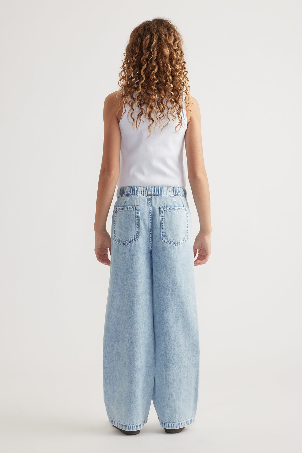 Girl seen from behind wearing a white tank top and light wash full length jeans