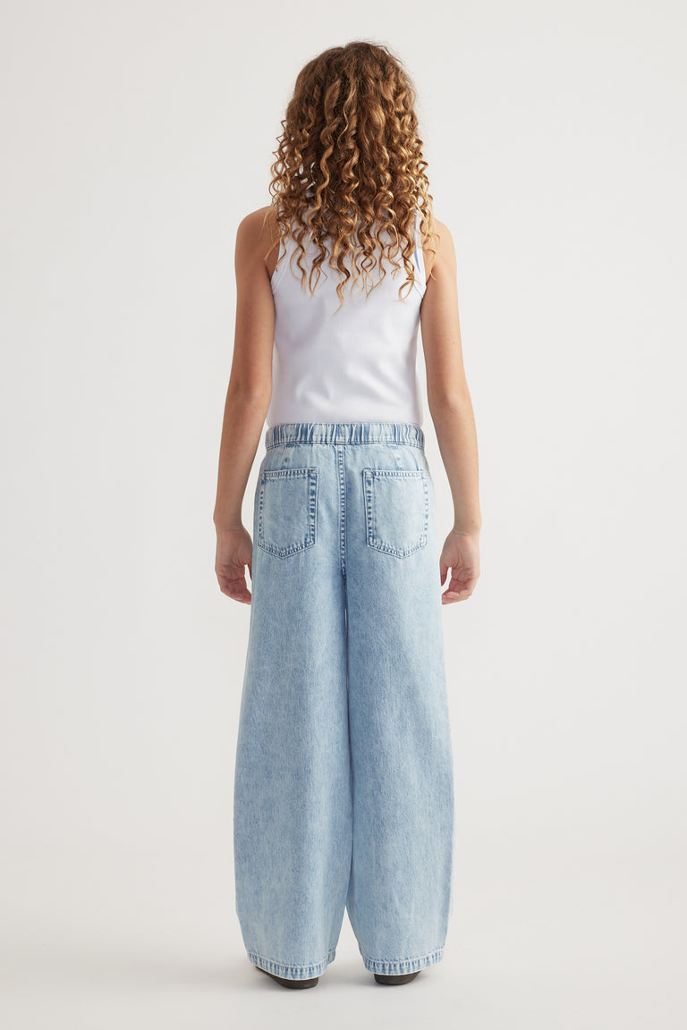 Girl seen from behind wearing a white tank top and light wash full length jeans