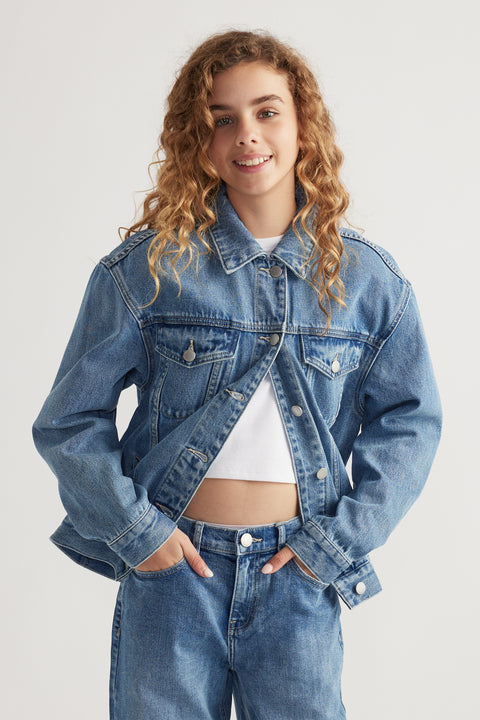 Teen girl smiling wearing oversized blue denim jacket over white cropped top and matching denim jeans