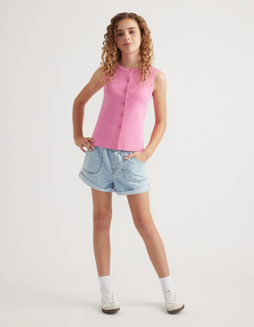 Girl wearing light wash denim pull-on shorts with rolled hems and a pink sleeveless top
