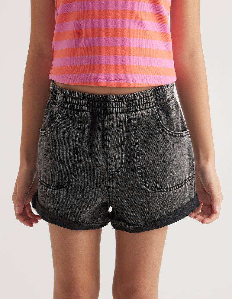 Girl wearing charcoal denim pull on shorts with an elastic waist, four pockets and cuffed hems