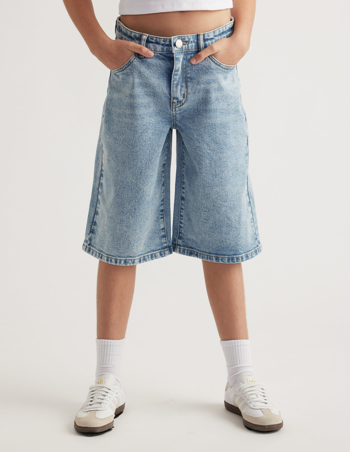 Girl wearing light wash wide leg denim jorts with a white cropped tee, socks and sneakers