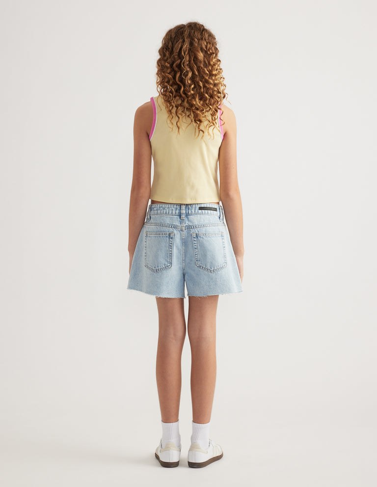 Back view of girl wearing light wash A line denim shorts with a yellow tank top and white sneakers