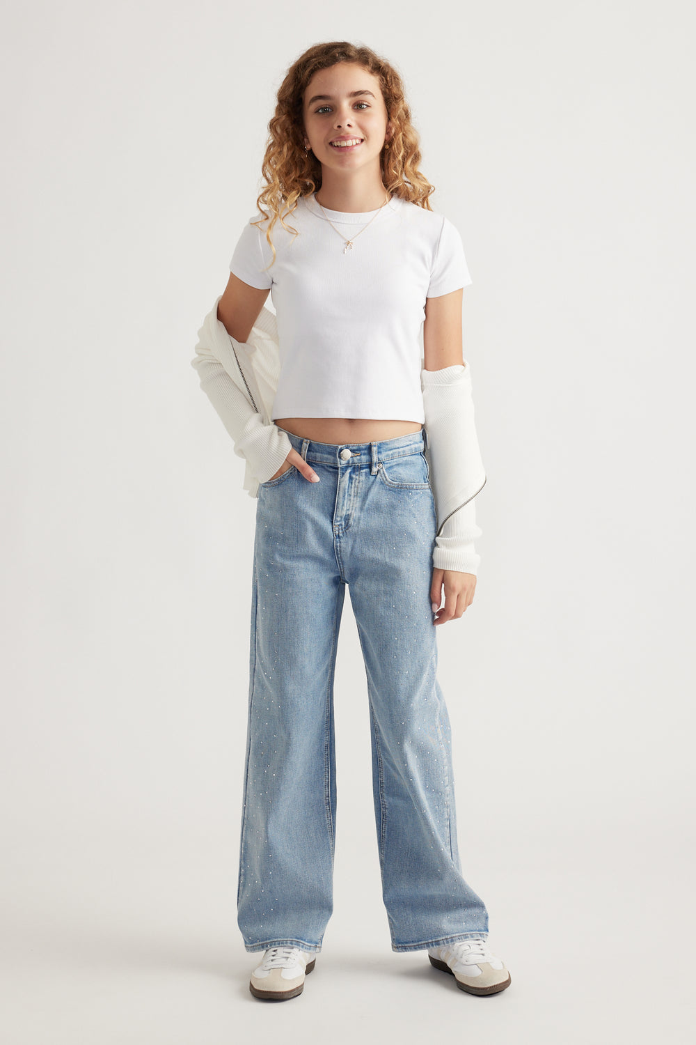 Teen girl wearing mid-rise light blue denim jeans with subtle crystal details paired with a white cropped tee