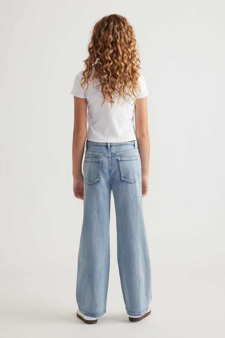 Rear view of teen girl wearing light blue wide-leg jeans with subtle crystal embellishments and white short sleeve top