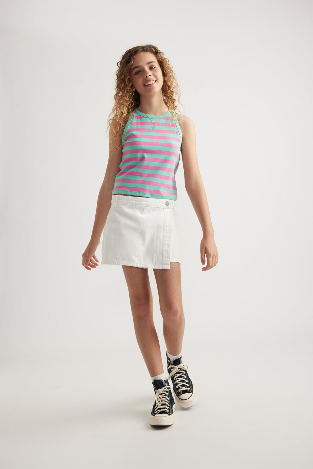 Girl wearing a pink and turquoise striped racer tank with a white skirt and black high top sneakers