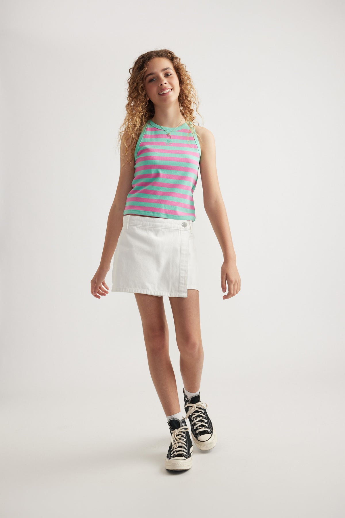 Girl wearing a pink and turquoise striped racer tank with a white skirt and black high top sneakers