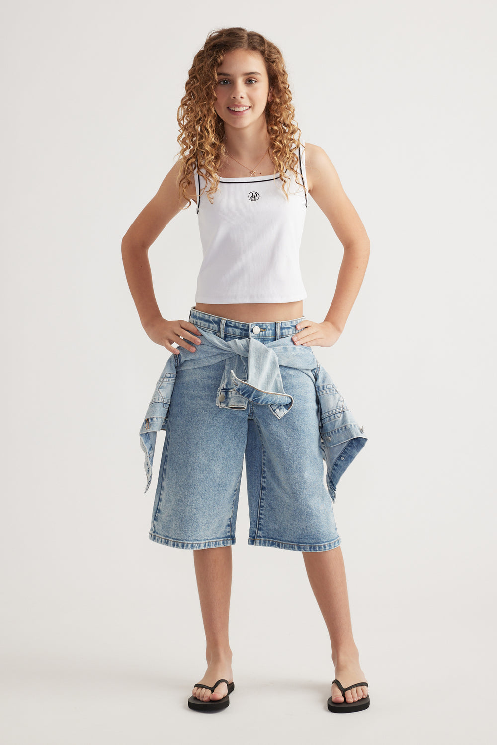 Girl wearing a white ribbed scoop neck tank, denim shorts and black sandals