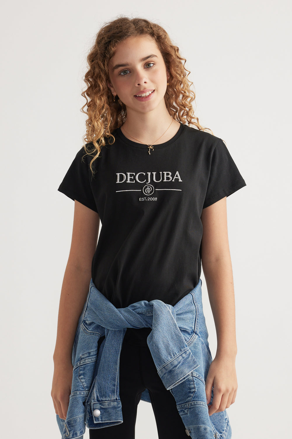 Girl wearing a black Decjuba heritage graphic T shirt with a denim jacket tied around her waist