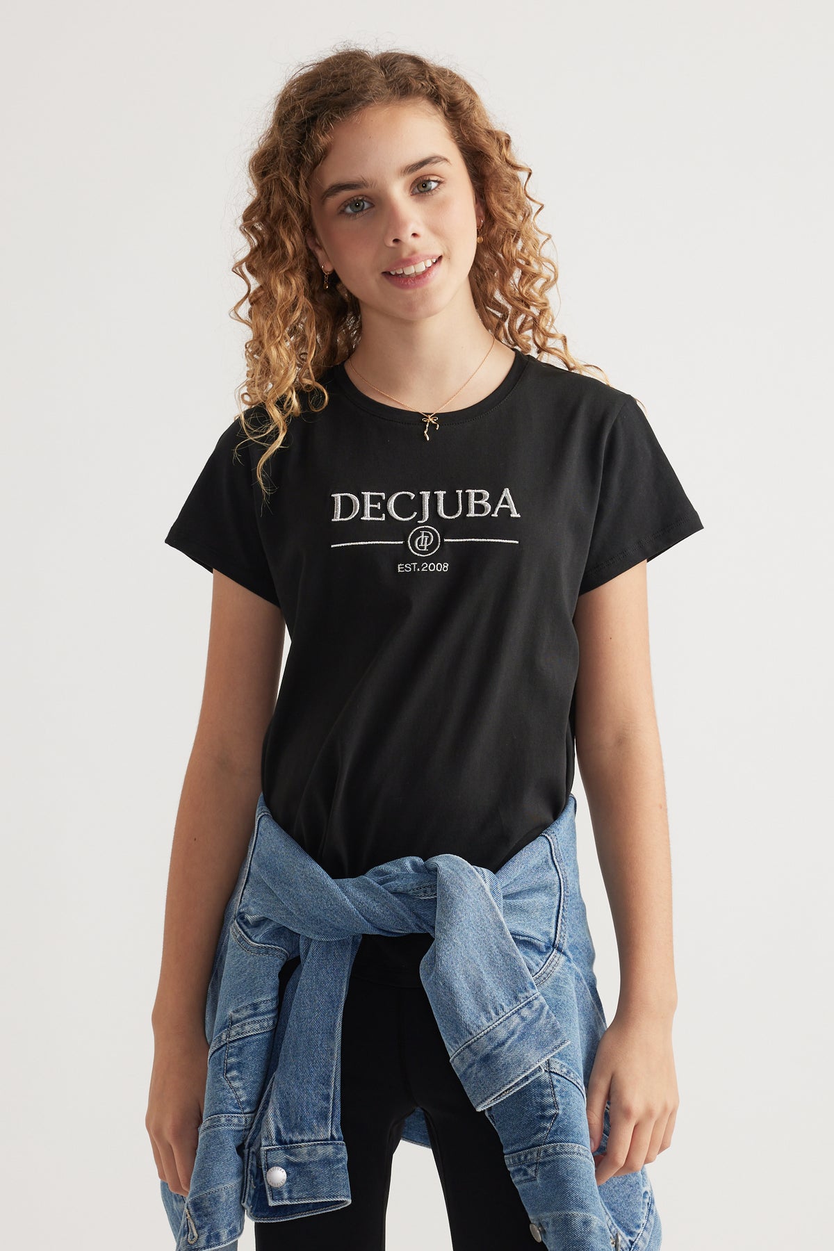 Girl wearing a black Decjuba heritage graphic T shirt with a denim jacket tied around her waist