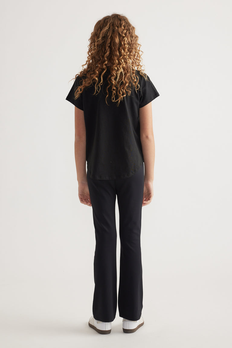 Back view of girl wearing a black heritage graphic T-shirt with black pants and sneakers