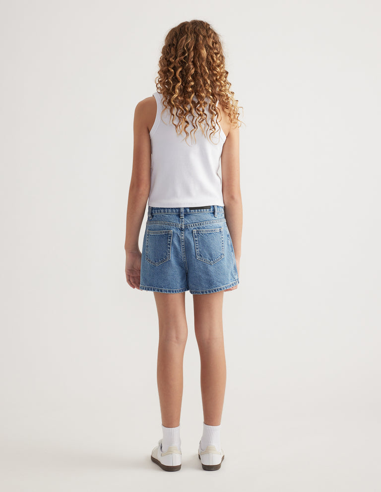 Back view of girl wearing a blue denim skort with a white tank top, ankle socks and sneakers