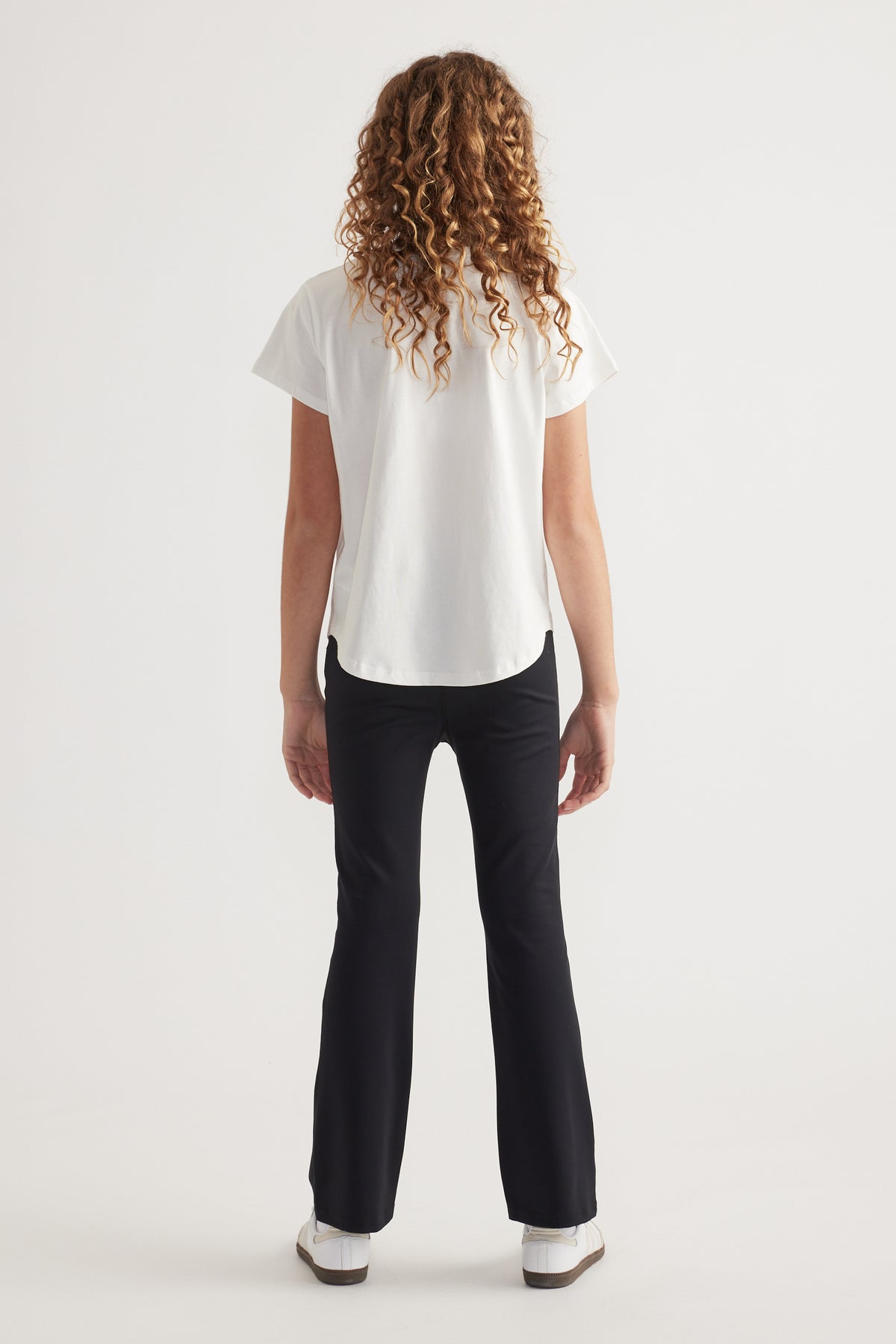 Back view of girl wearing a white crew neck T-shirt with black pants and sneakers