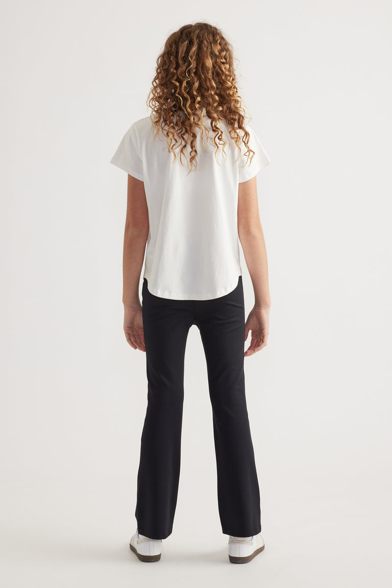 Back view of girl wearing a white crew neck T-shirt with black pants and sneakers