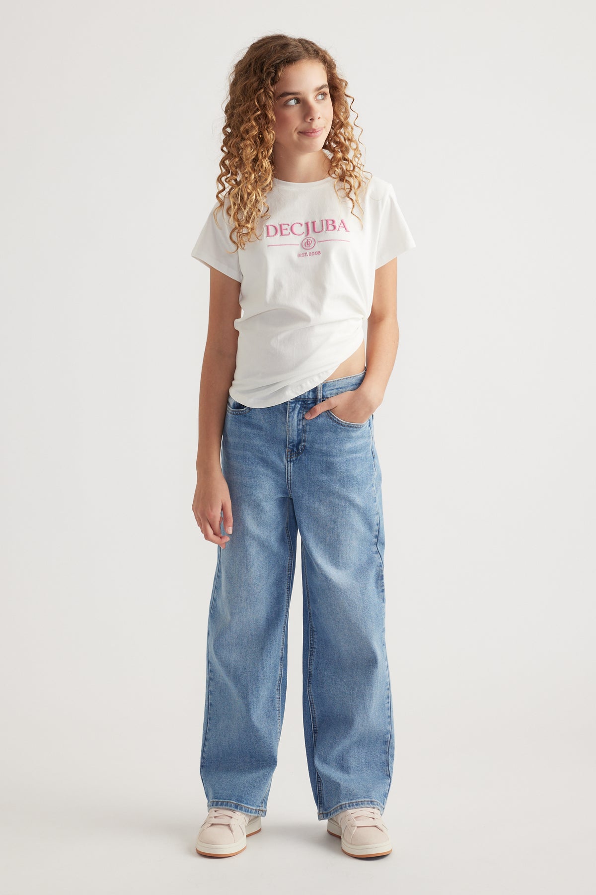 Girl wearing a white DECJUBA heritage graphic tee with wide leg blue jeans and sneakers