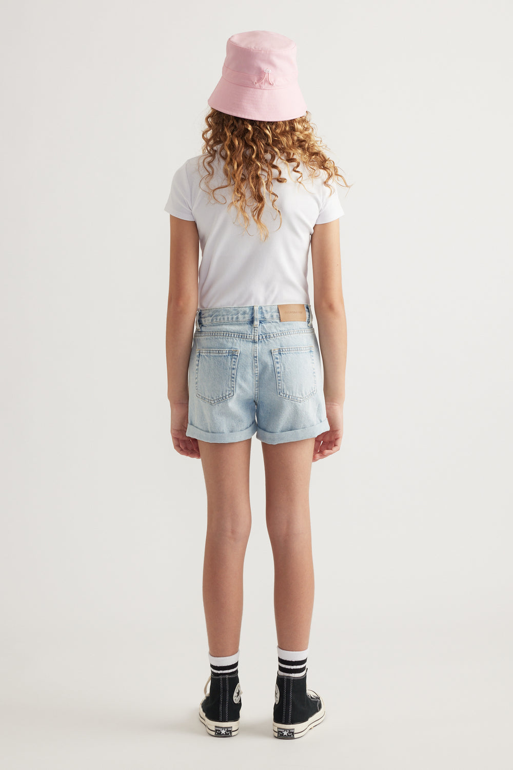 Back view of a girl wearing crystal denim shorts, a white tee, pink bucket hat and black sneakers